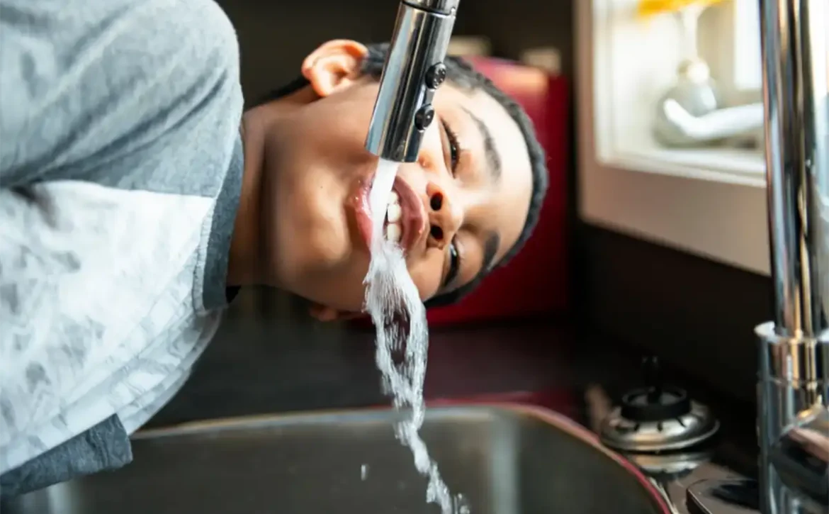 A young boy drinking from the kitchen faucet