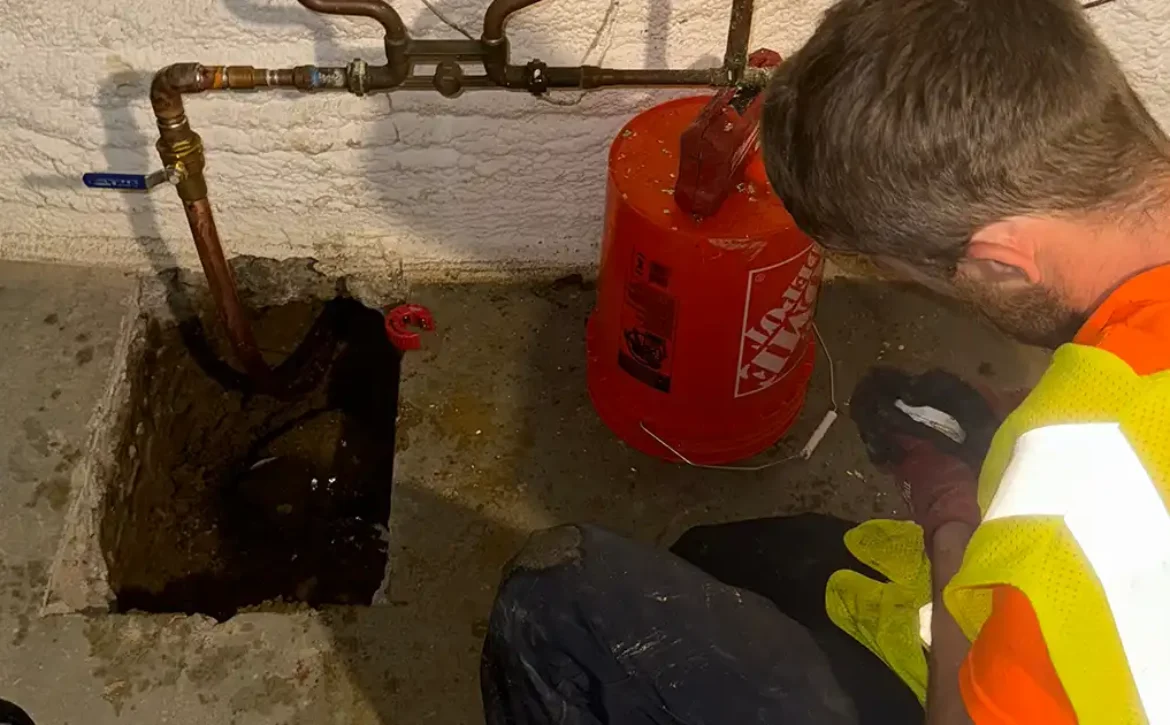 A utility technician completes the connection of a newly installed copper service line with the existing interior plumbing of a residential basement.